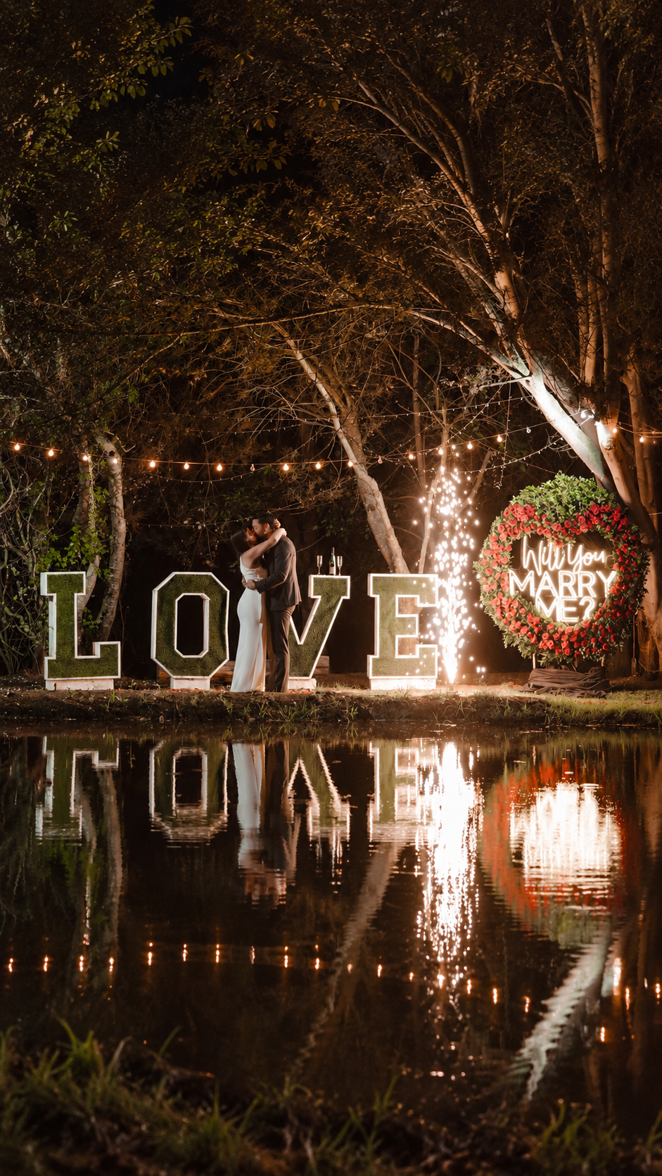 Elanie y Christian abrazados durante su propuesta de matrimonio, junto al lago y las luces